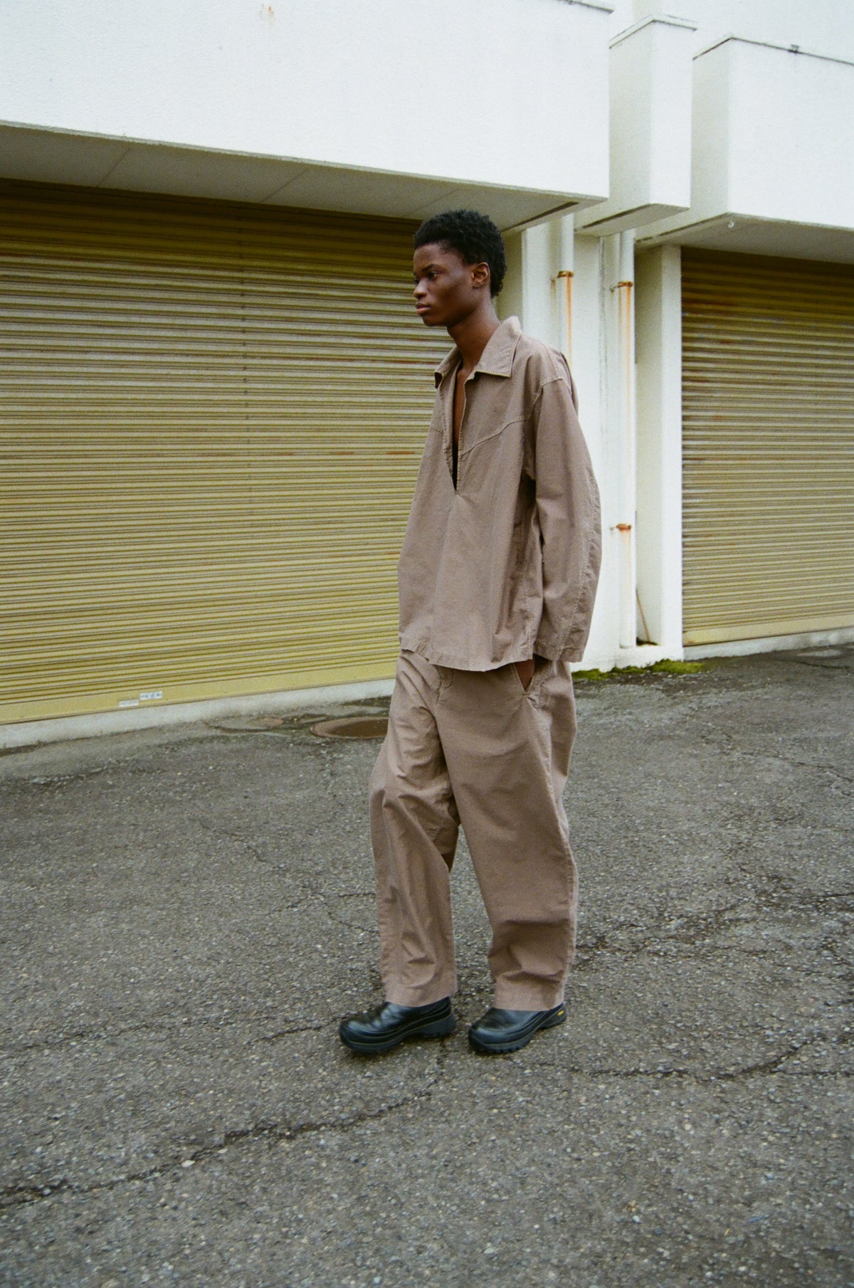 concause WIDE TAPERD SLACKS ルックスタイリング / TAUPE 男性モデル 屋外シャッター前 セットアップ サイドビュー
