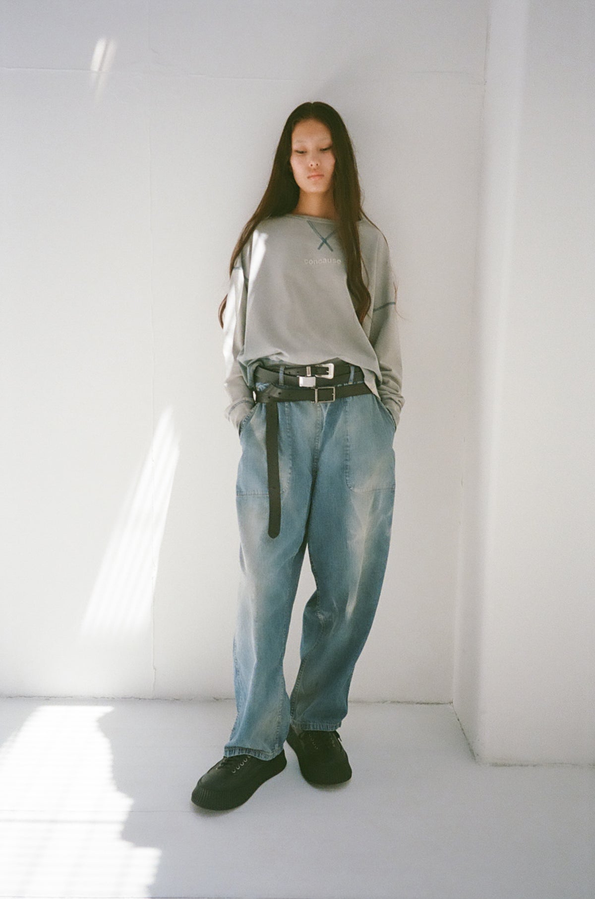 concause SUN FADE PINTER PANTS ルックスタイリング / INDIGO 女性モデル 白い室内壁 ベルト着用 グレーロンT重ね着 フロントビュー 全体像
