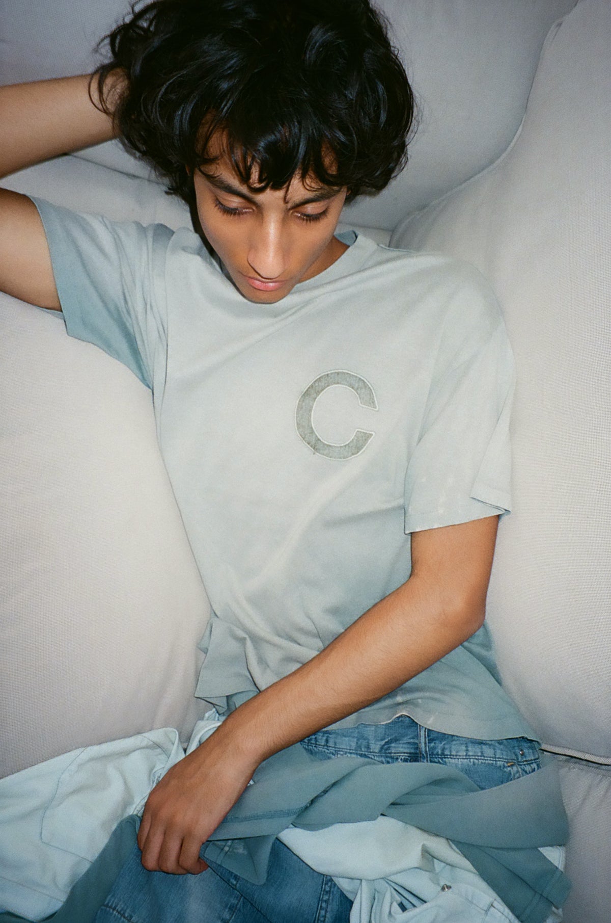 concause C LOGO FADE TEE ルックスタイリング / BLUE 男性モデル ソファ 横たわりポーズ デニム重ね着 上半身クローズアップ 俯瞰アングル
